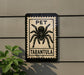 A sign with a black and white illustration of a tarantula, mounted on a wall.