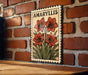 A framed illustration of red lilies is displayed on a brick wall, with the word "AMARYLLIS" written above the flowers.