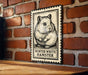 A metal sign featuring a hamster illustration is mounted on a brick wall.