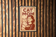 A sign with the text "CAT MOM" and an illustration of a woman holding a cat.