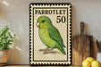 A vintage-style postage stamp featuring a green parrot, with the number 50 printed on it. The stamp is displayed on a shelf next to a wooden cutting board and some kitchen utensils.