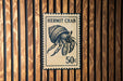 A Hermit Crab postage stamp is displayed on a wooden wall.