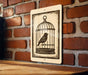 A sign featuring a bird in a cage is mounted on a brick wall.
