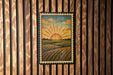 A framed illustration of a sunrise over a field is displayed on a wooden wall.