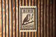 A sign that reads "BIRD SINGING" with a bird illustration and musical notes, mounted on a wooden wall.
