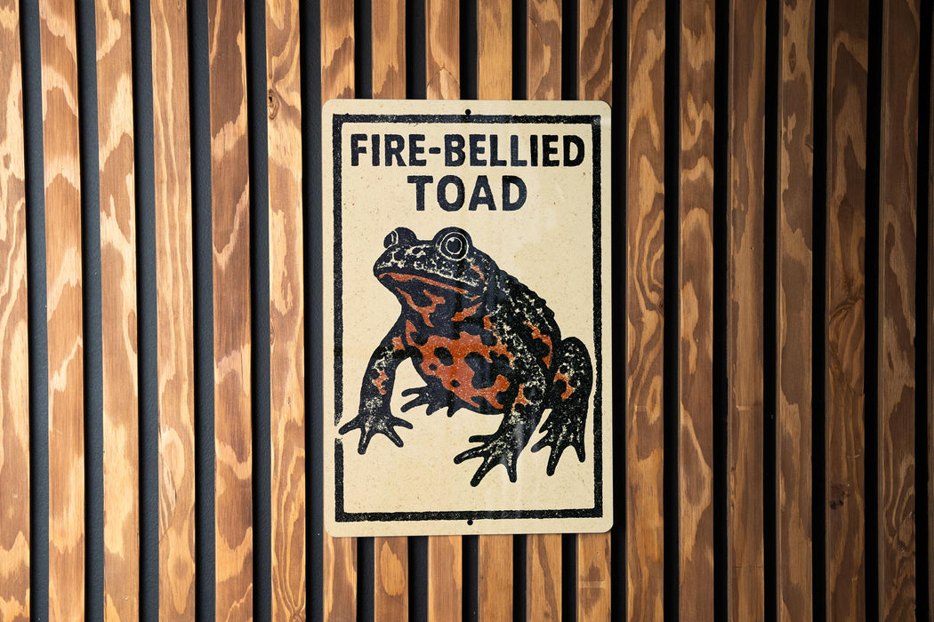 a sign with a picture of a fire-bellied toad on it, mounted on a wooden wall.