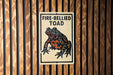 a sign with a picture of a fire-bellied toad on it, mounted on a wooden wall.
