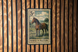 A vintage-style stamp depicting a horse in a pastoral setting, mounted on a wooden wall.
