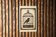 A sign with a bird inside a cage is displayed against a wooden background.