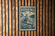 A vintage-style metal sign with a kayaker illustration, mounted on a wooden wall.