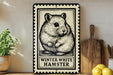 A metal sign with a black and white illustration of a hamster, accompanied by the text "WINTER WHITE HAMSTER" on a wooden shelf.