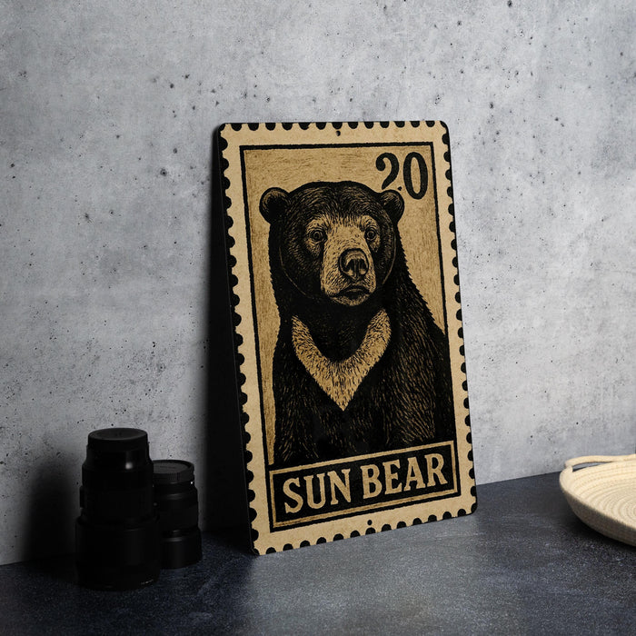A wooden postcard featuring a black bear illustration, with the text "SUN BEAR" printed on it, is displayed on a table next to some black camera lenses.