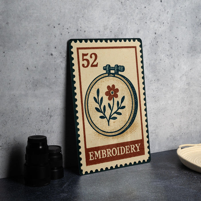 a vintage-style stamp or postcard with an embroidery design, placed on a table next to some black camera lenses.