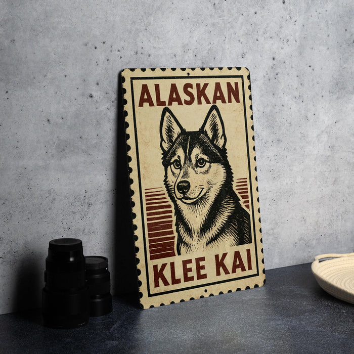 A metal sign with a picture of a husky dog and the text "ALASKAN KLEE KAI" on it, placed on a countertop next to some black camera lenses.