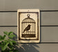 a sign with a bird inside a cage, placed on a wall next to a plant.