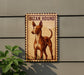 a brown and white hound dog standing on a wall, with a plant to the left of the dog.