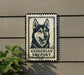 a sign with a picture of a dog, specifically a Gerberian Shepsky, mounted on a wall.