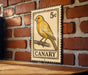 A vintage-style metal sign featuring a yellow canary perched on a branch, mounted on a brick wall.