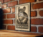 A metal sign featuring a chinchilla illustration is mounted on a brick wall.
