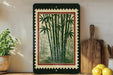 a framed print of bamboo plants on a shelf, with a wooden cutting board and a potted plant nearby.