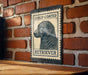 A metal sign with a curly-coated retriever illustration is mounted on a brick wall.