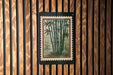 a framed print of bamboo plants hanging on a wooden wall.