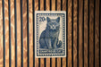 A blue and white postage stamp featuring a cat, mounted on a wooden wall.