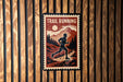A vintage-style metal sign with the text "TRAIL RUNNING" and an illustration of a person running on a trail through a mountainous landscape.