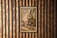 A wooden wall with a framed illustration of a rabbit sitting at a table, holding a teapot and a cup, with the text "RABBIT AT TEA PARTY" on the frame.