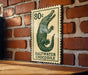 A green and white postage stamp featuring a crocodile is displayed on a brick wall.