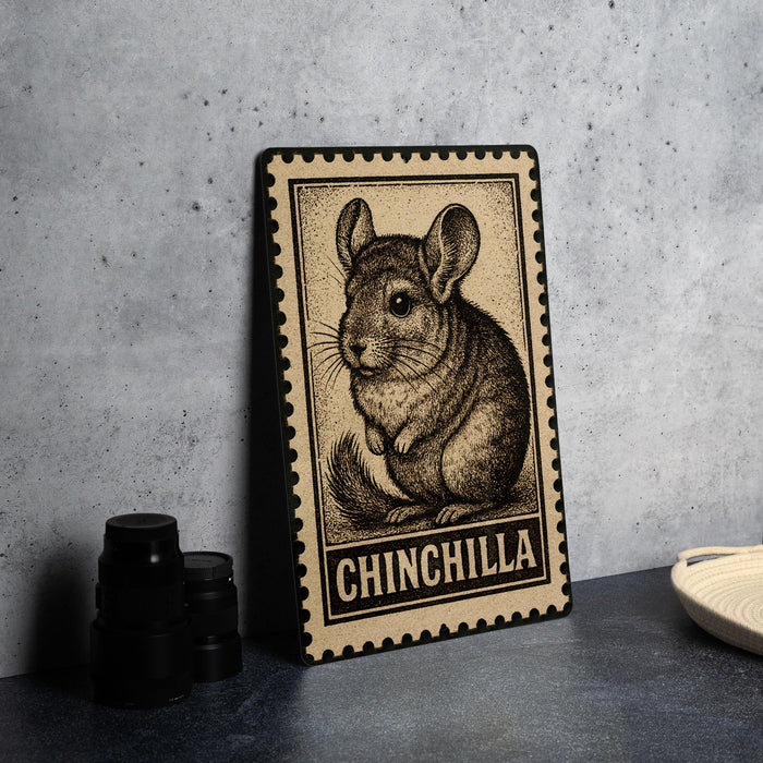 A framed illustration of a chinchilla is displayed on a table, with a stack of black camera lenses and a white plate visible in the background.