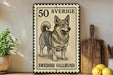 A framed Swedish Vallhund dog stamp is displayed on a shelf, with a potted plant and kitchen utensils visible in the background.