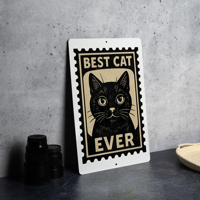 A metal sign with a black cat illustration and the text "BEST CAT EVER" is displayed on a table.