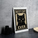 A metal sign with a black cat illustration and the text "BEST CAT EVER" is displayed on a table.