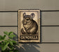 a chinchilla, a small rodent, on a sign with the word "CHINCHILLA" written below it.