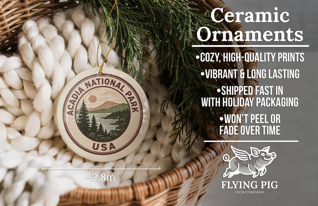 Ceramic ornaments, featuring a circular ornament with the text "ACADIA NATIONAL PARK USA" and a pine tree design, are displayed in a woven basket.