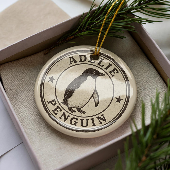 A circular ornament with the name "ADELIE PENGUIN" printed on it, surrounded by a decorative border.