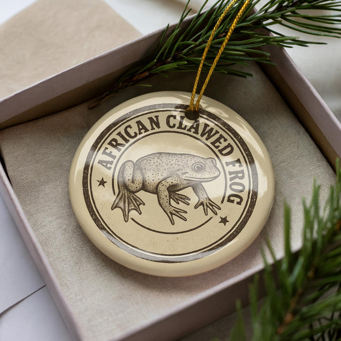 A circular ornament with a printed image of an African clawed frog, surrounded by a decorative border.