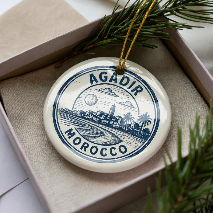 A decorative ornament in a box, featuring a circular design with a cityscape and palm trees, along with the text "AGADIR MOROCCO".