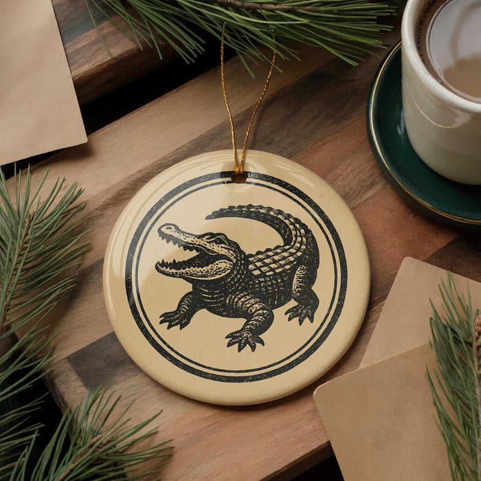 a round ornament with a black and white illustration of a crocodile on a wooden surface, surrounded by pine branches and a cup of coffee.