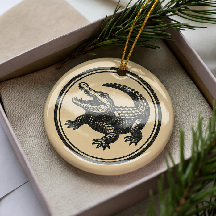 A ceramic ornament in the shape of a crocodile is displayed in a box, surrounded by pine branches.