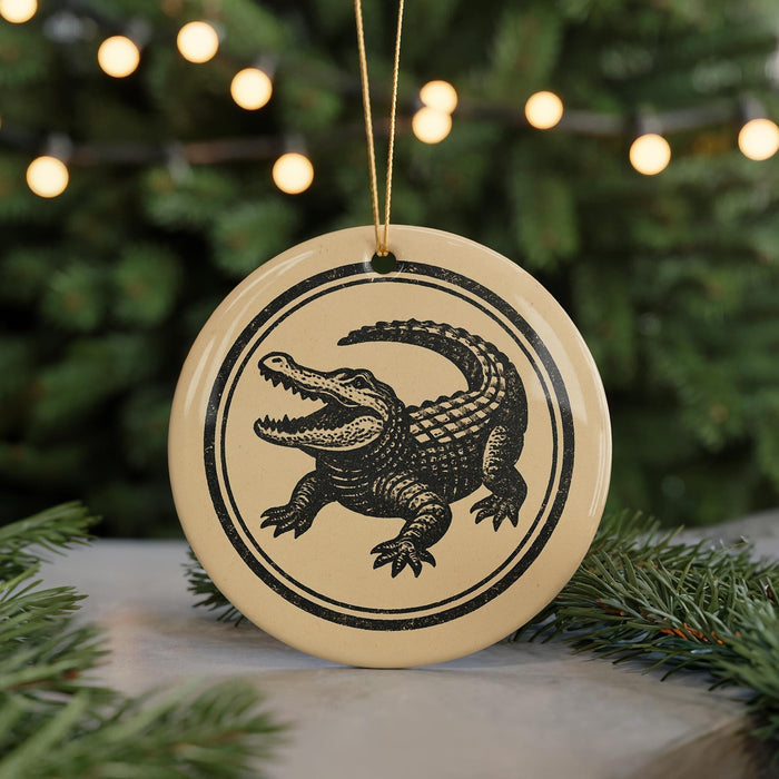 A round ornament featuring a black and white illustration of a crocodile is displayed in front of a Christmas tree with twinkling lights.
