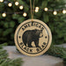 A circular ornament featuring a black bear image and the text "AMERICAN BLACK BEAR" is displayed in front of a blurred Christmas tree.