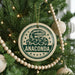 A Christmas tree decorated with ornaments, including a round ornament with a snake design and the word "ANACONDA" printed on it.