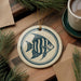 a round ceramic ornament with a fish design, placed on a wooden surface alongside a cup of coffee and some pine branches.