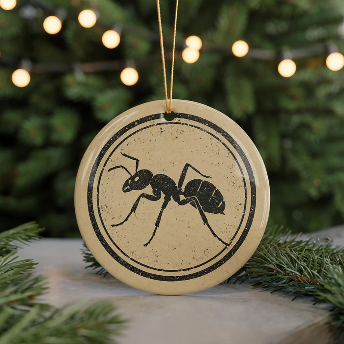 A round ornament with a black ant illustration on it, hanging from a string.
