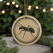 A round ornament with a black ant illustration on it, hanging from a string.