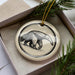A ceramic ornament in a box, featuring a black and white illustration of an animal, likely a bear or a similar creature.