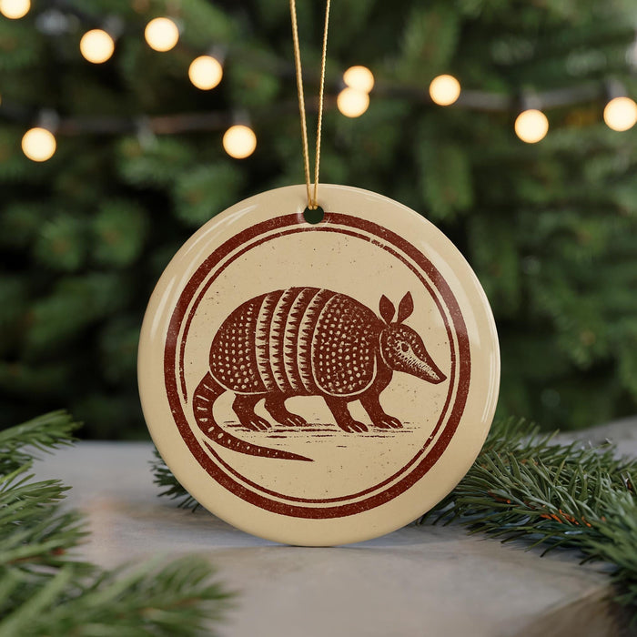 A round ornament featuring an armadillo design is displayed in front of a Christmas tree with twinkling lights.