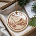 A circular ornament with a sailboat and a castle in the background, hanging from a string.